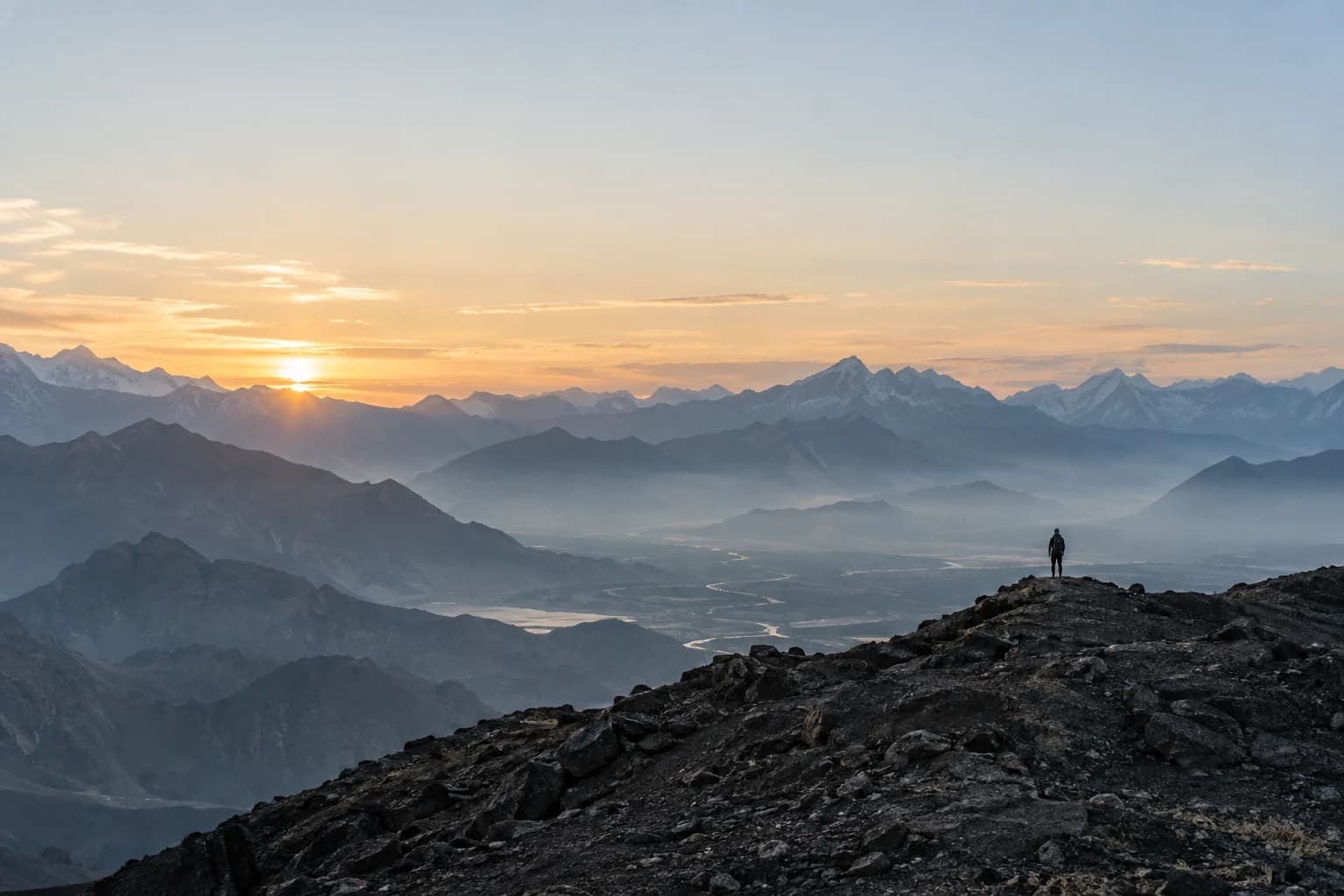 A person looking across a vast mountain horizon at dawn